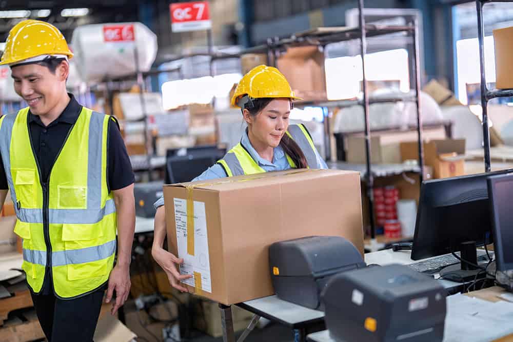 Two workers in safety vests and hard hats are working in a warehouse. | Unlimited Solutions