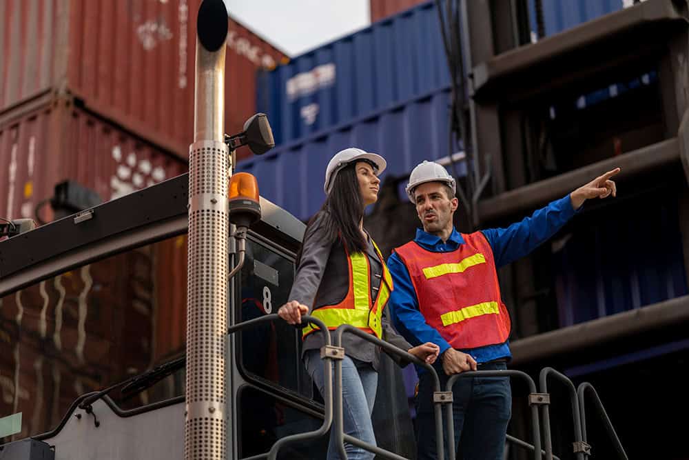 Two people standing on a truck with a container in the background. | Unlimited Solutions