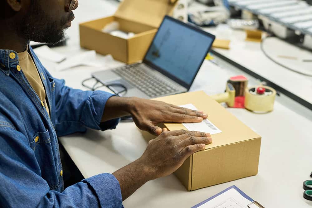 A man is working on a laptop while holding a box. | Unlimited Solutions