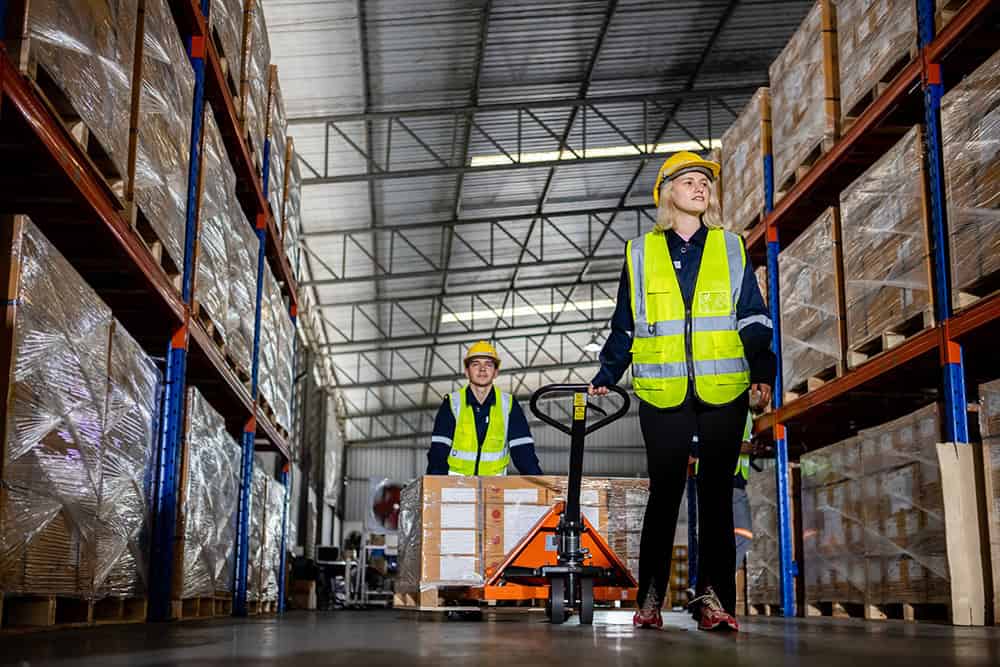 Two workers in safety vests are walking in a warehouse. | Unlimited Solutions