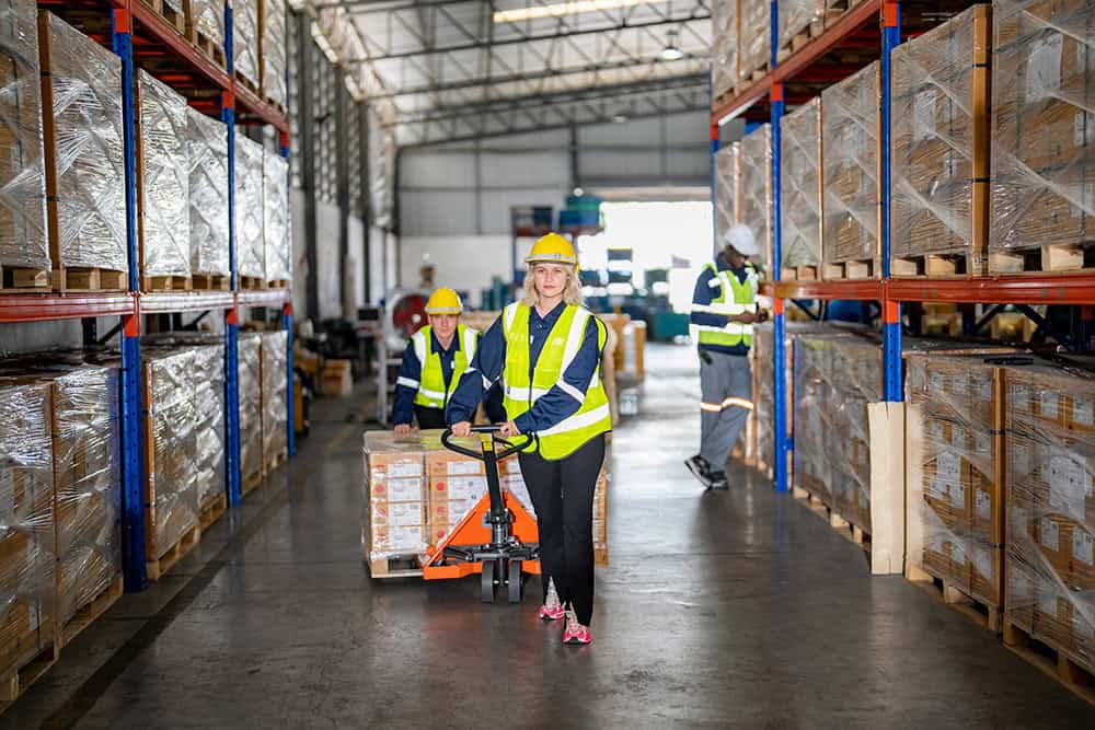 A woman in a safety vest and hard hat is pushing a cart in a warehouse. | Unlimited Solutions